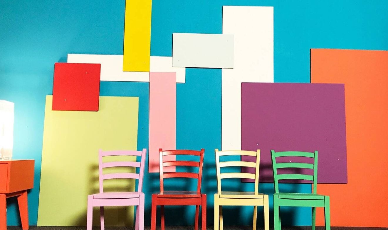 Four colourful chairs are placed in front of a bright patchwork wall in a photo studio